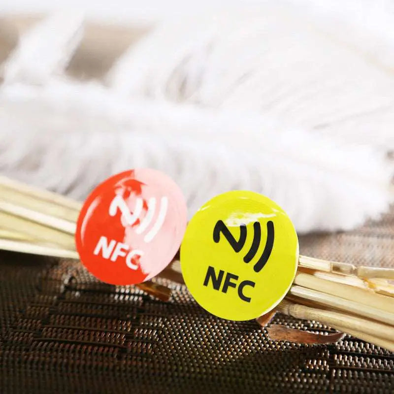 Roter und gelber metallresistenter runder NFC-Aufkleber mit NFC-Symbol und Schriftzug, auf geflochtenem Untergrund.