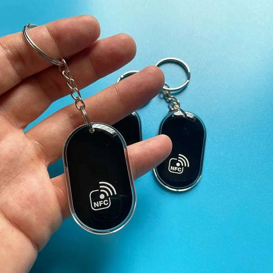 Schwarzer NFC-Schlüsselanhänger mit ovaler Form und silbernem Rand, in Hand gehalten.