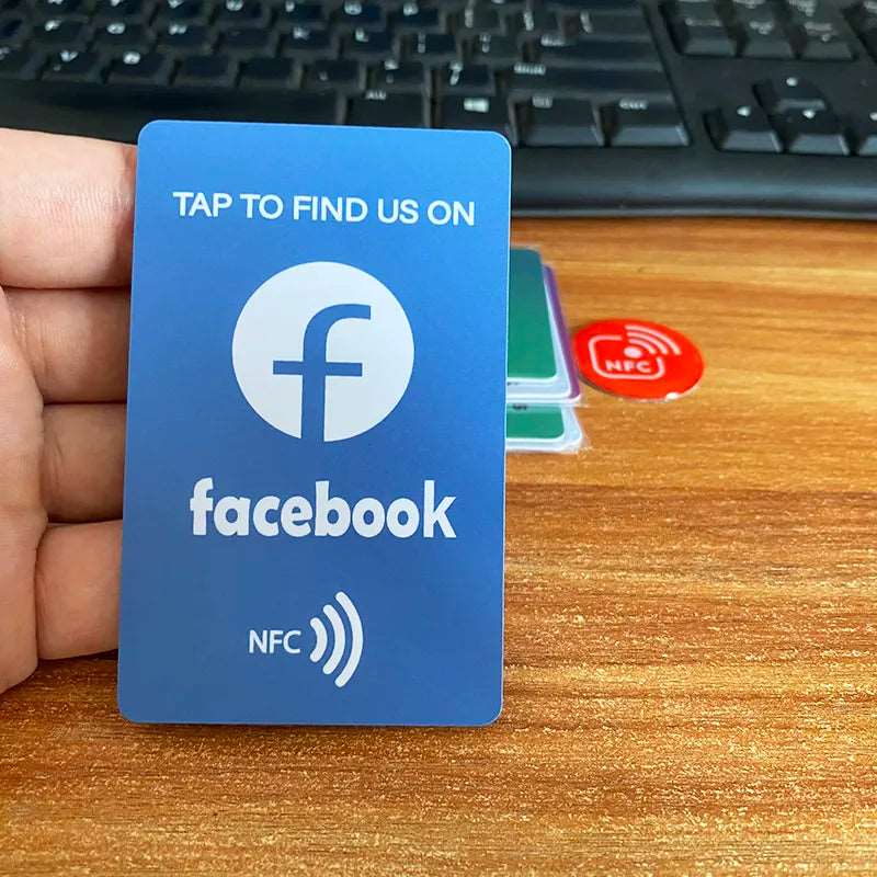 Blauweiße NFC-Karte mit Facebook-Logo und Text "Tap to find us on Facebook" vor Tastatur.